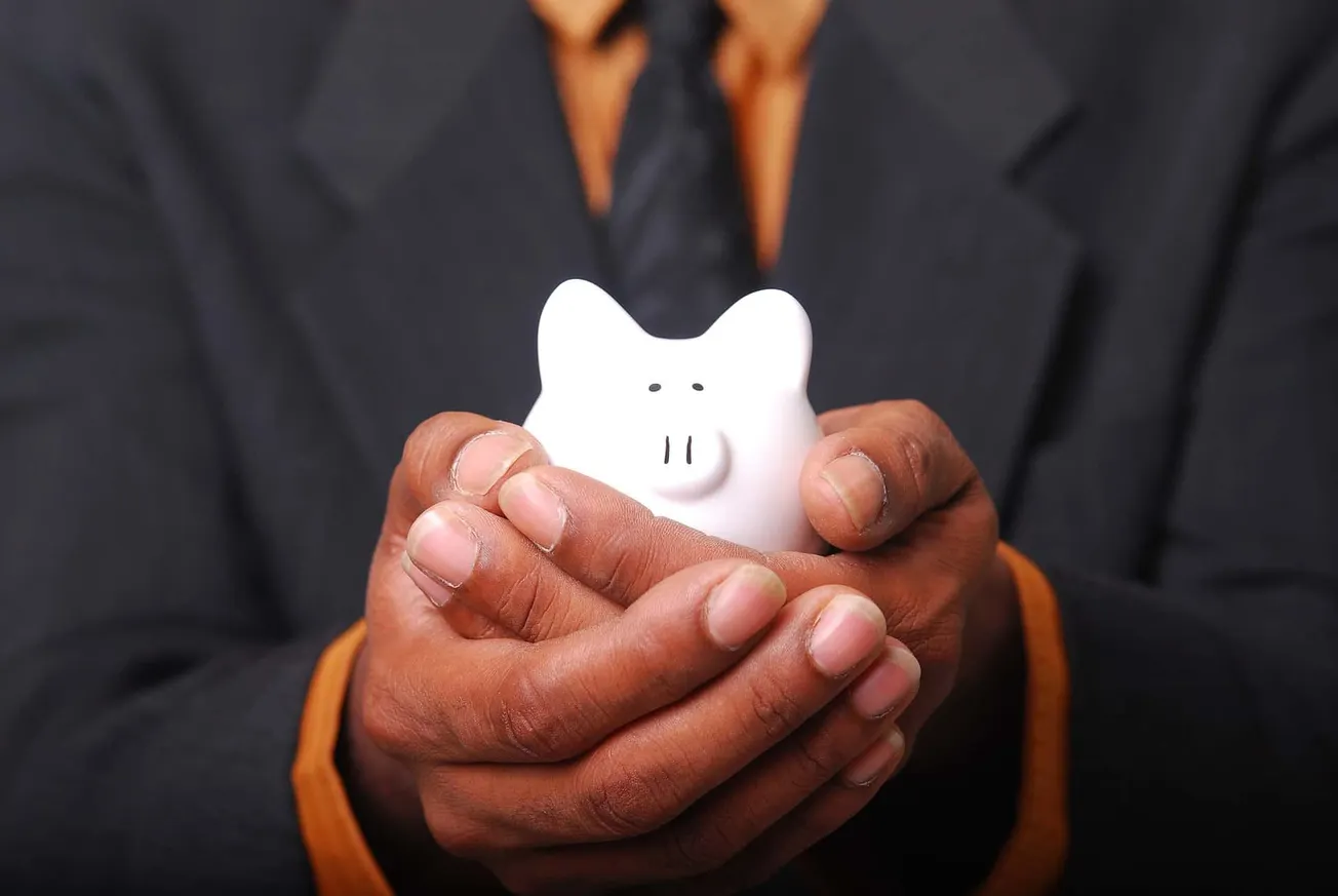 Saving money in a ceramic piggy bank held by a person in a business suit for financial planning, savings, or investment conce