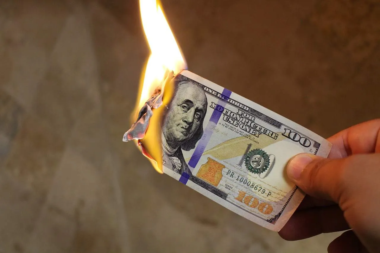 Burning $100 US dollar bill as a symbol of money loss or financial risk.