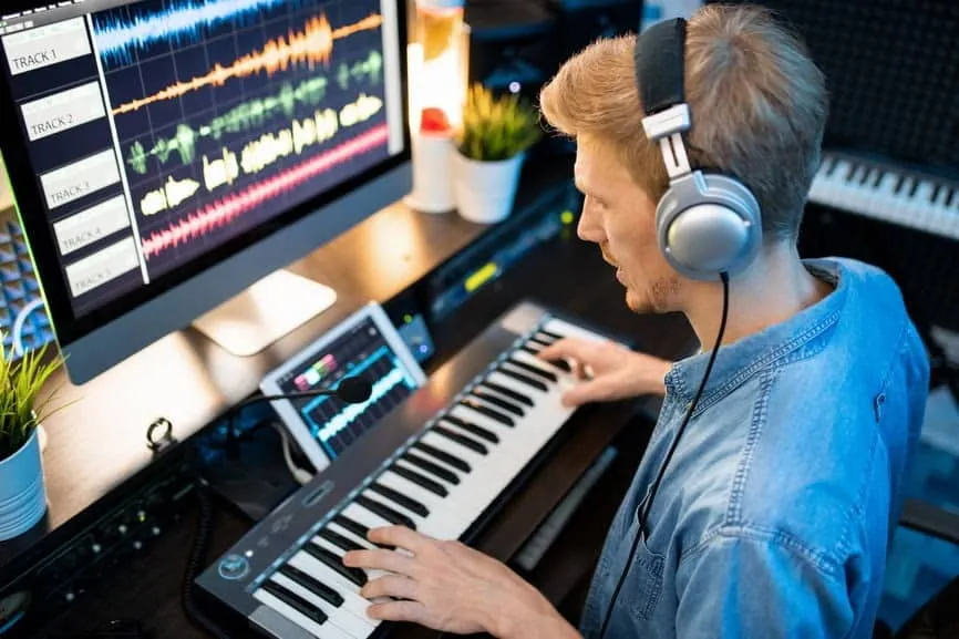 Music producer working on digital audio workstation with keyboard and headphones in home studio, creating music tracks with p