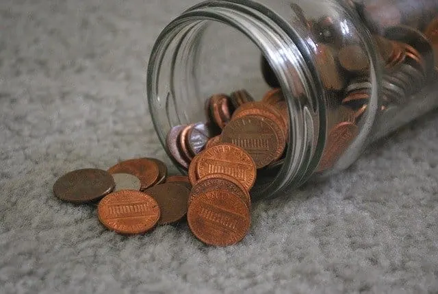 Jar of loose pennies spilling onto a gray surface, symbolizing savings, coins, or financial concepts.