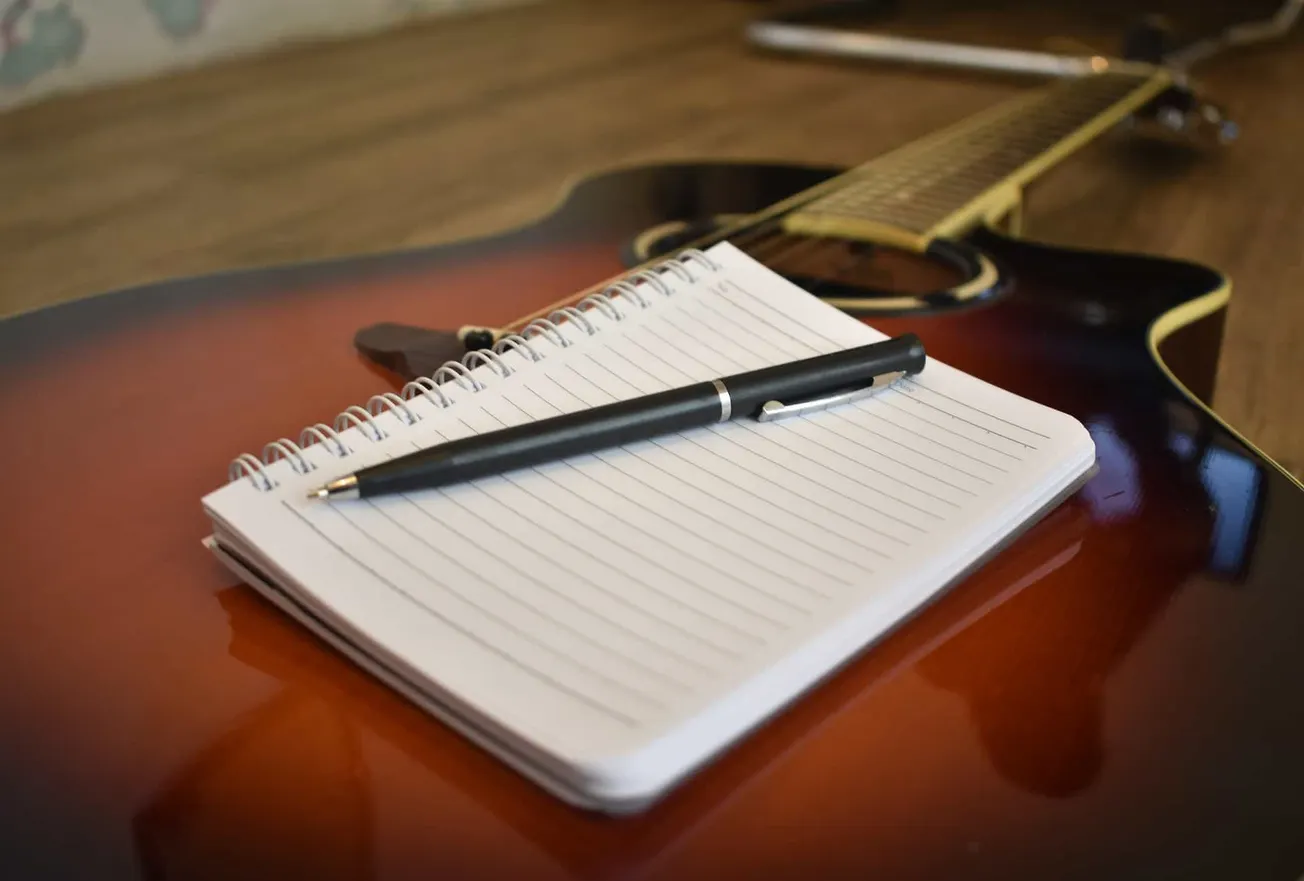Sheet of lined paper with a black pen on an acoustic guitar; musical planning or songwriting concept.