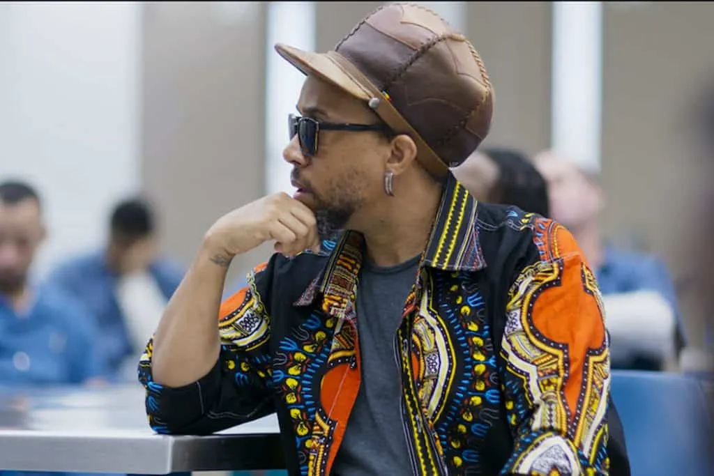 Stylish man wearing sunglasses and a colorful patterned jacket, sitting in an audience at a conference or event, with a focus