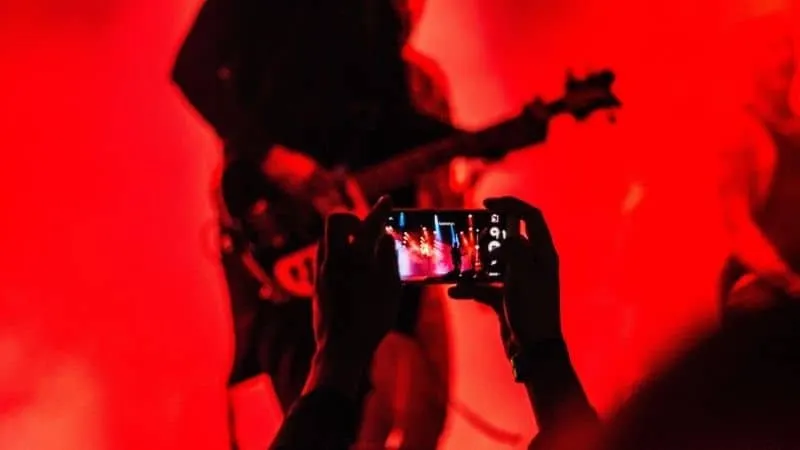 A person capturing a live music performance with a smartphone during a concert, vibrant red lighting creates an energetic atm