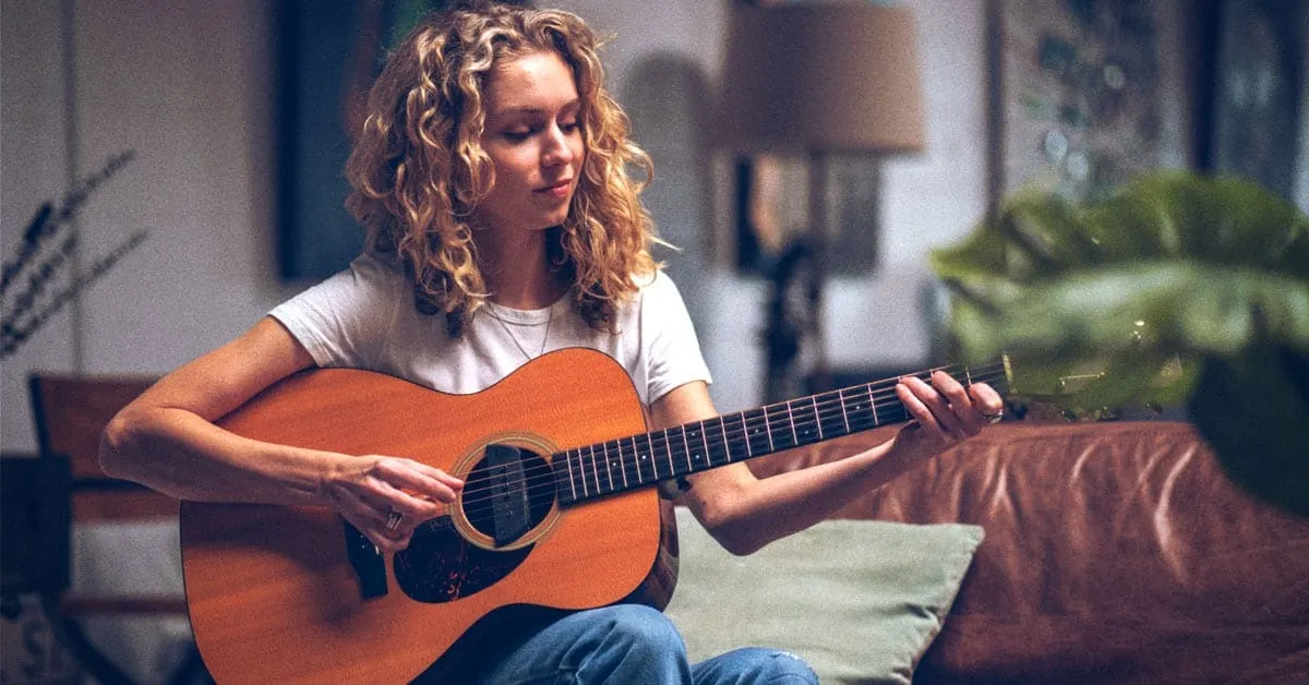 Relaxed young woman playing acoustic guitar in cozy home setting, practicing music, showcasing musical talent, and creating a