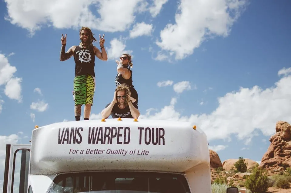 Vans warped tour group on top of a bus in a desert landscape with rocky formations and blue sky with clouds, promoting music
