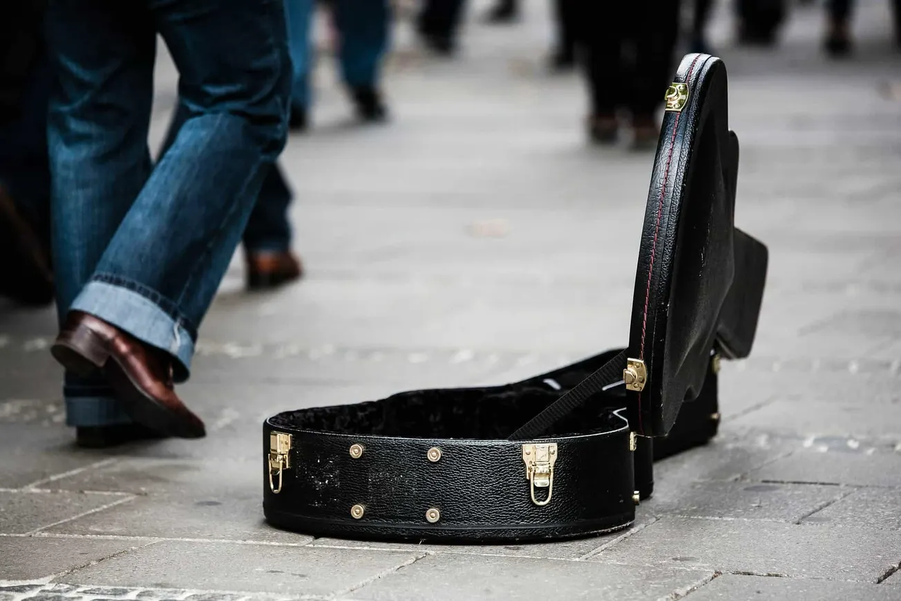 A suitcase with a guitar inside left on the sidewalk, people walking by in the background, street scene, urban environment, c