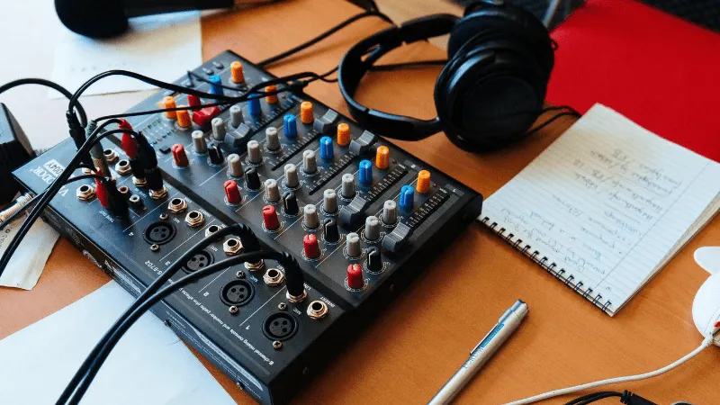 Audio mixing console with headphones, notebook, and pen on a wooden desk for music production and podcasting.