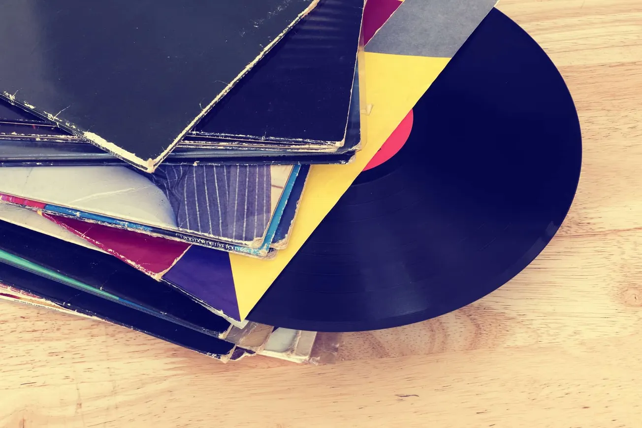 Vintage vinyl records with colorful album covers and a black turntable on a wooden surface.