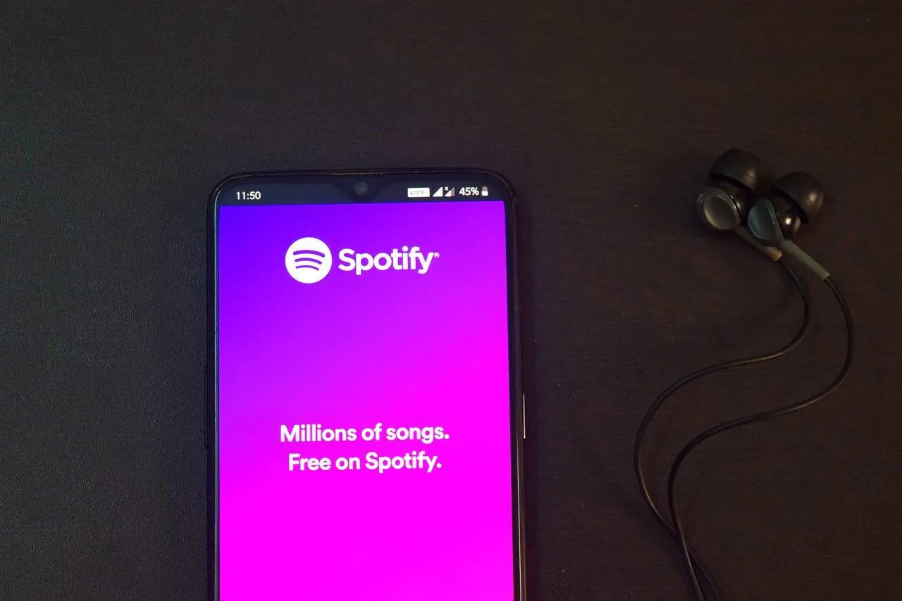 Spotify app on smartphone with wireless earphones, showcasing music streaming service.