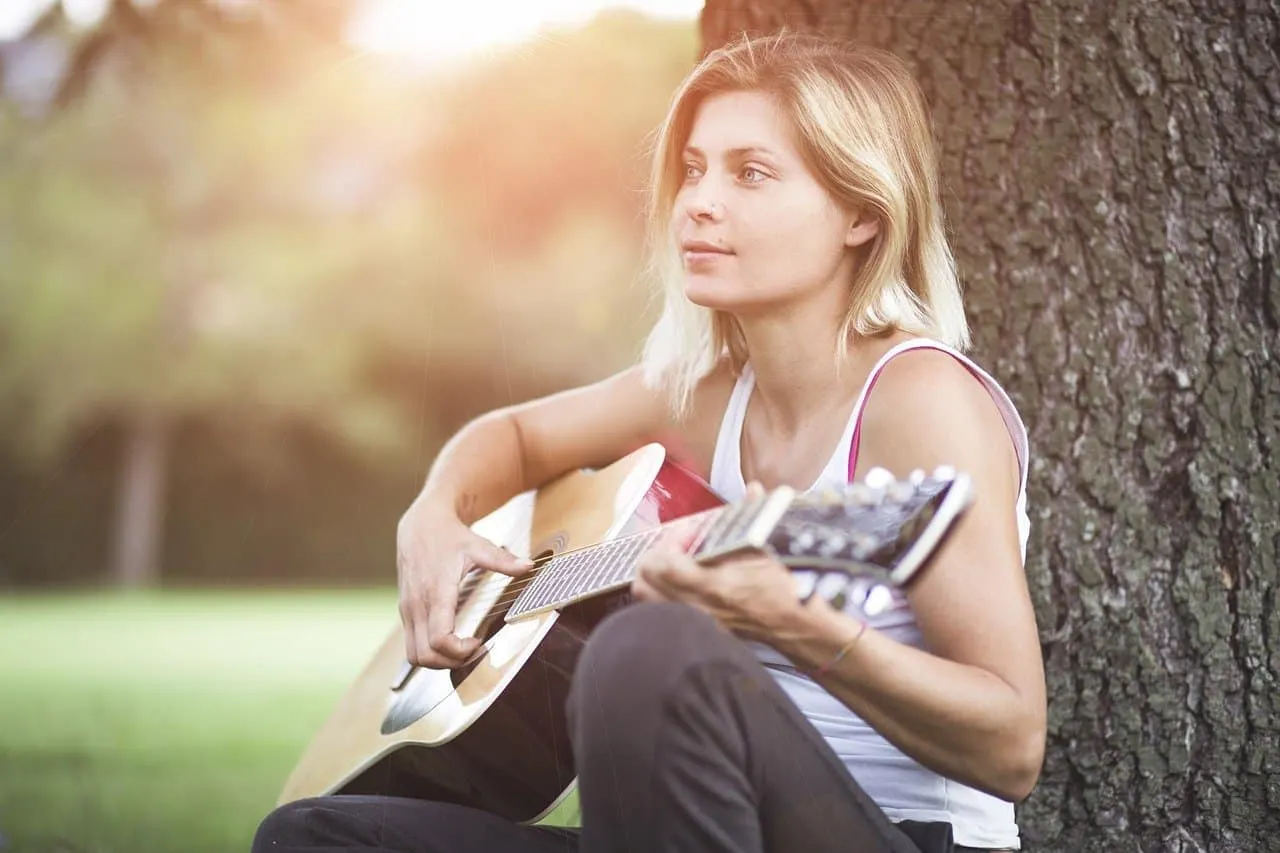 Girl playing acoustic guitar outdoors in park during sunset, relaxing music session, young woman with blonde hair, casual clo