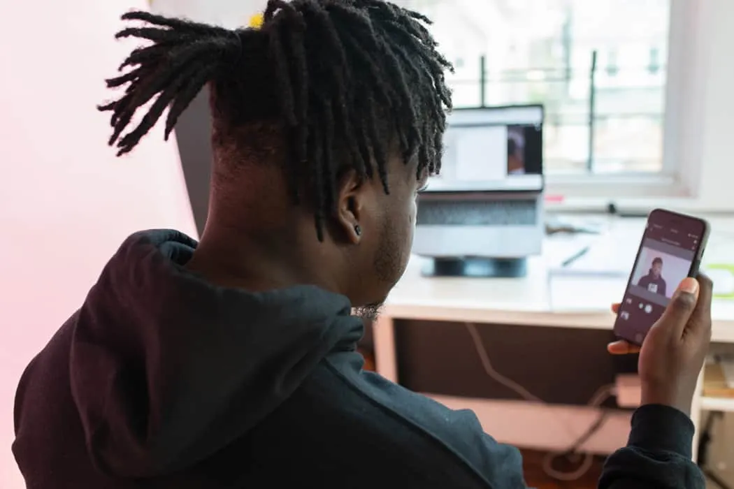Boy taking selfie with smartphone at home or studio computer setup, casual clothing, modern technology, social media, remote