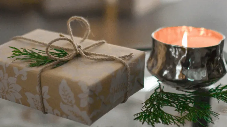 A beautifully wrapped holiday gift with a sprig of pine and a lit candle, creating a cozy festive atmosphere perfect for Chri
