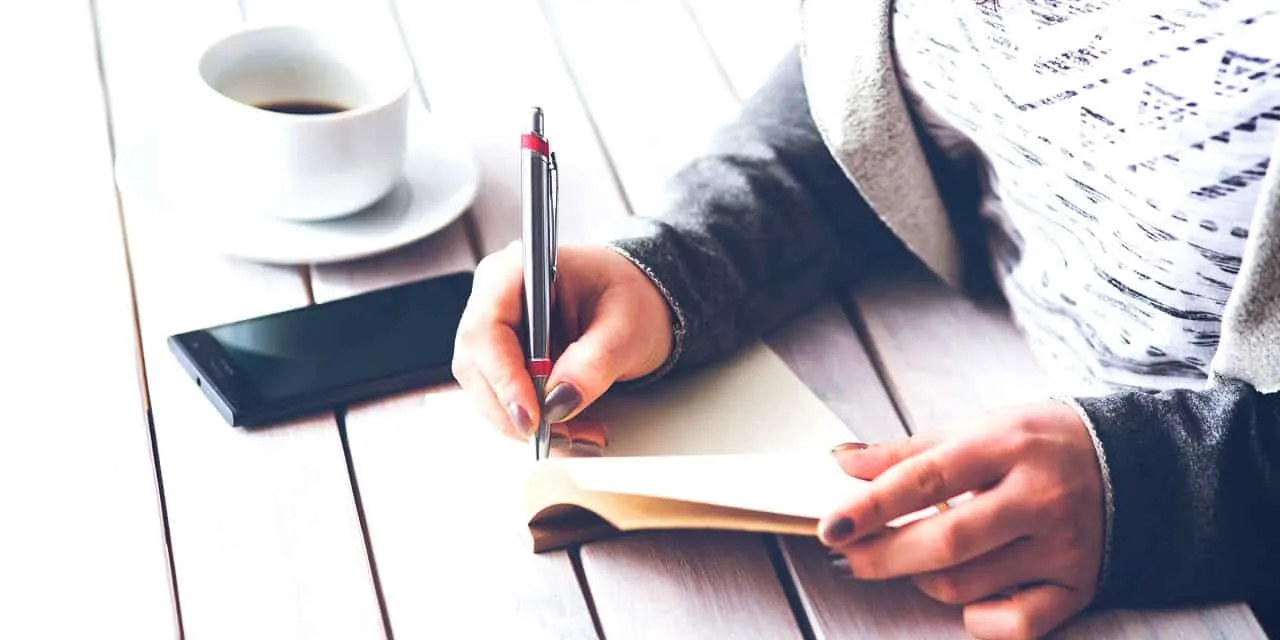Laptop, smartphone, coffee cup, and notebook on wooden table — modern workspace for content creation and digital marketing.