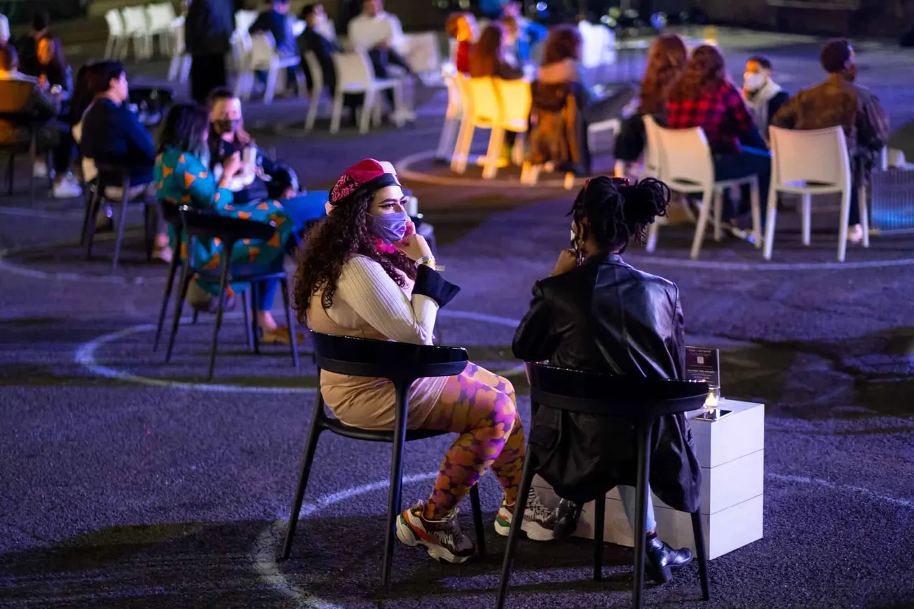 Pandemic outdoor social gathering with people wearing masks, diverse group, nighttime event, social distancing, vibrant light