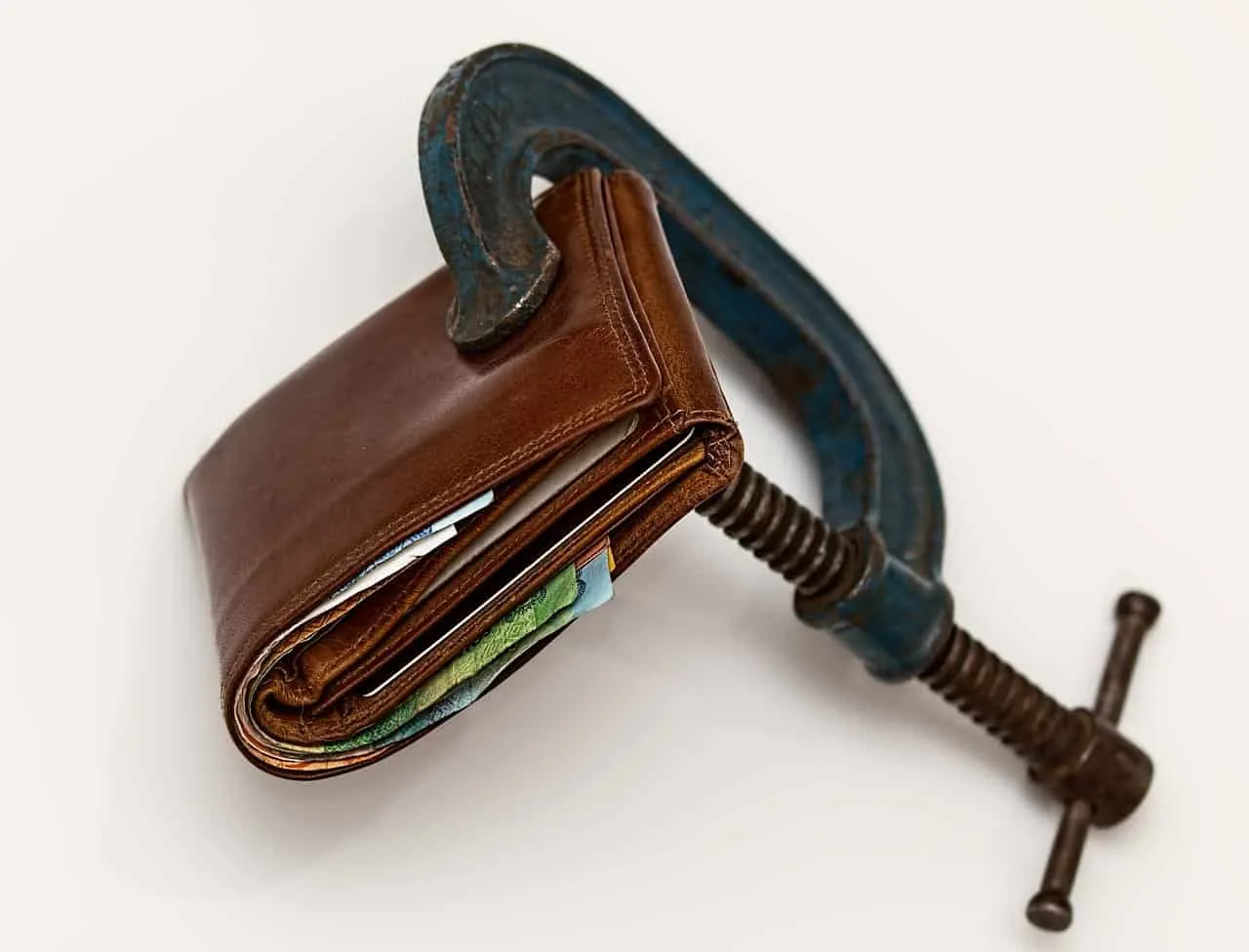 Wallet with banknotes and credit cards clamped in a blue C-clamp, symbolizing financial pressure or banking issues.