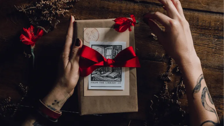 Hand wrapping a gift with a red ribbon on a rustic wooden surface, surrounded by decorative paper shreds, highlighting holida