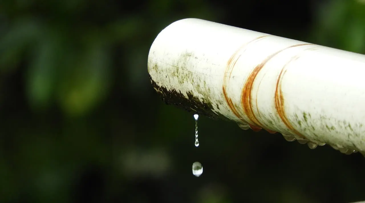 Fallen rainwater drip from a weathered white PVC pipe with rust stains, close-up shot, natural background, emphasizing water