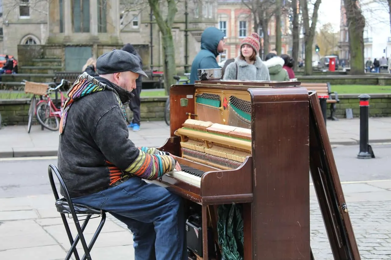 Vintage outdoor street piano player performing in a park during daytime in fall season.