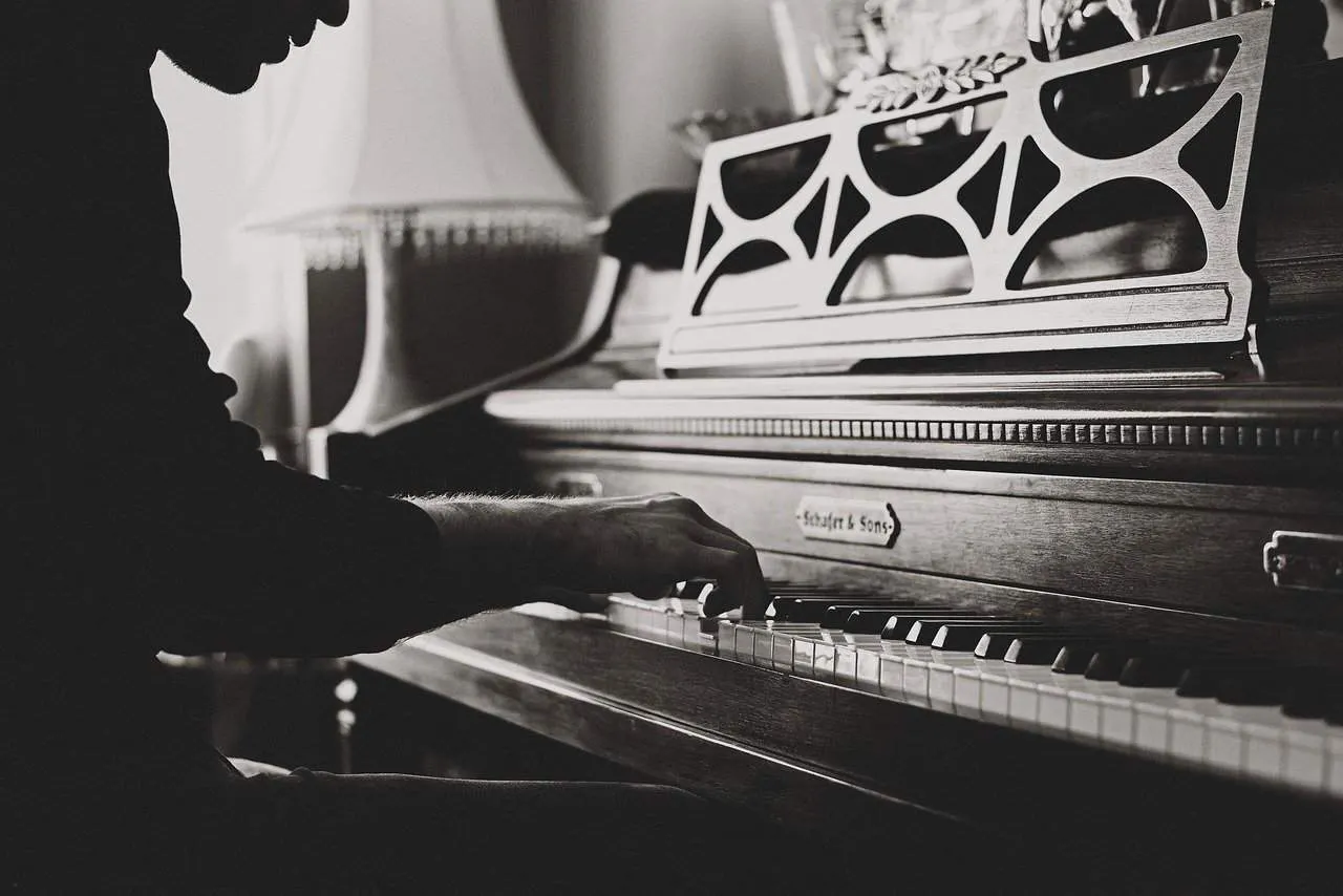Piano player playing a classical Schwarzschild & Son upright piano in a cozy indoor setting, black and white photo emphasizin
