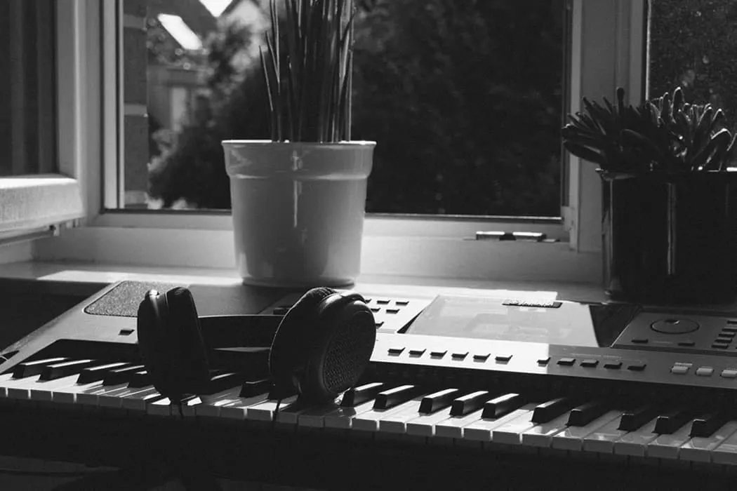 Keyboard with headphones on piano keys inside a home studio, natural light, plants on windowsill, inspiring music creation en