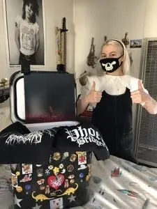 A woman wearing a face mask giving two thumbs up in a music studio with electronic equipment and a laptop.