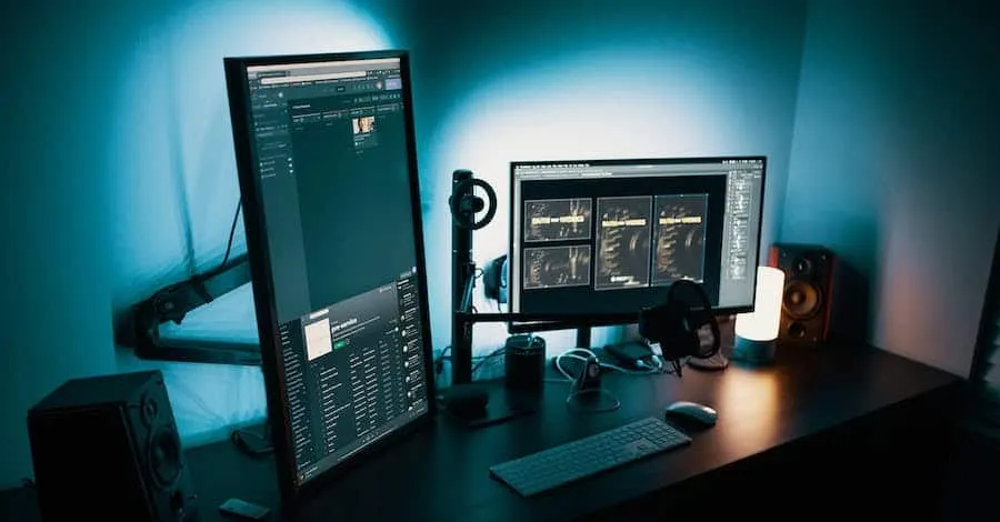 Dual computer monitors with music production software setup in a dimly lit home studio, showcasing digital audio workstations