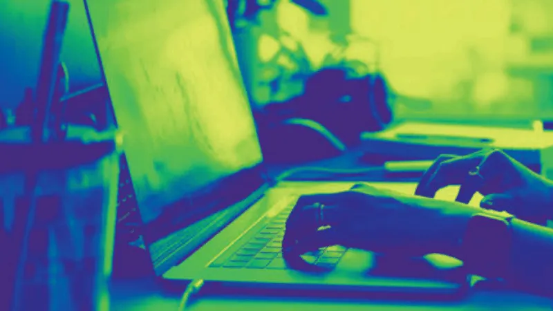 Vibrant green and blue-toned image of a person working on a laptop, highlighting digital music production, online music indus