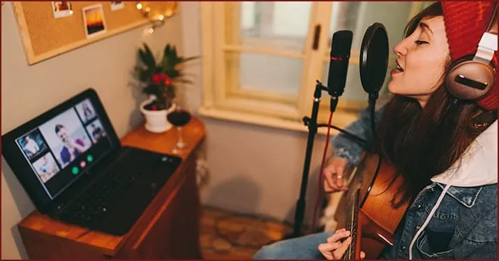 A young woman recording music with a microphone and headphones during a virtual performance from home.