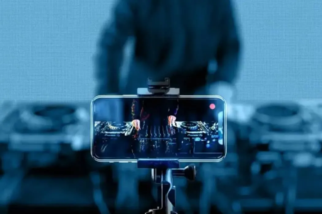 DJ mixing music in a club with live streaming on a smartphone for digital music promotion.