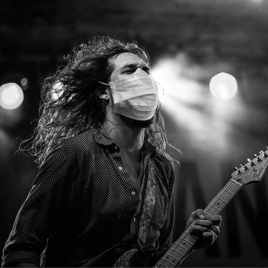 Woman playing electric guitar wearing face mask at concert or music event, black and white photo, live music performance, mus