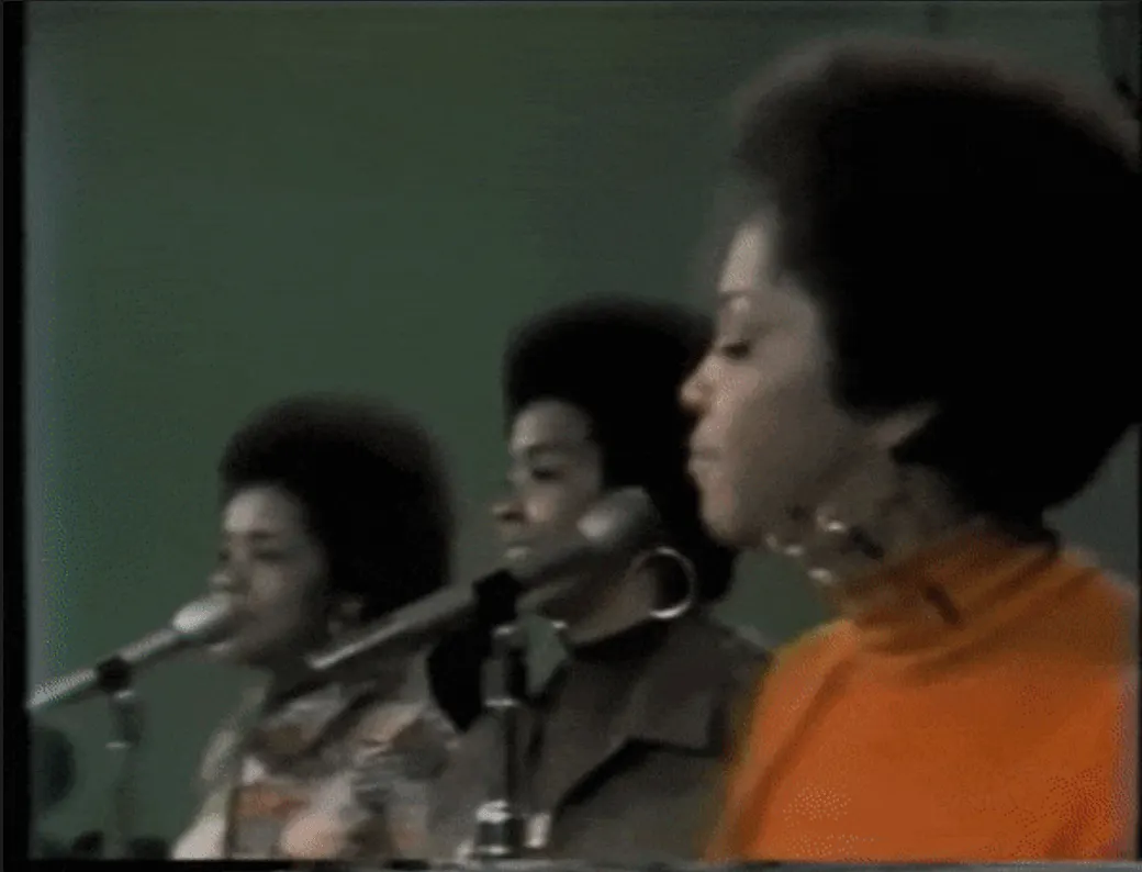 Recording of Motown female vocalists singing into microphones in a studio, vintage black-and-white video, 1960s music perform