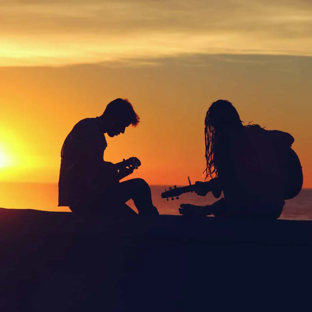 Young musicians playing guitars during sunset on the beach, capturing a moment of musical collaboration and creativity in a s