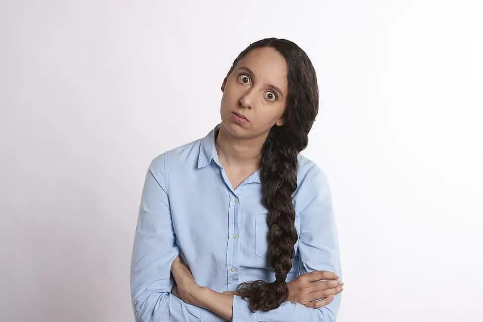 Confused woman with long braided hair wearing a light blue shirt, looking puzzled and confused, expressing uncertainty or cur