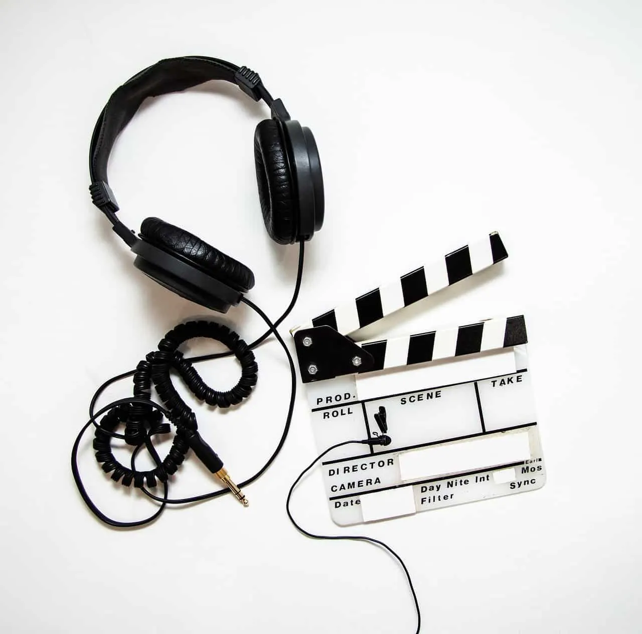 Headphones and film slate on white background for music production or film editing, highlighting audio-visual media creation