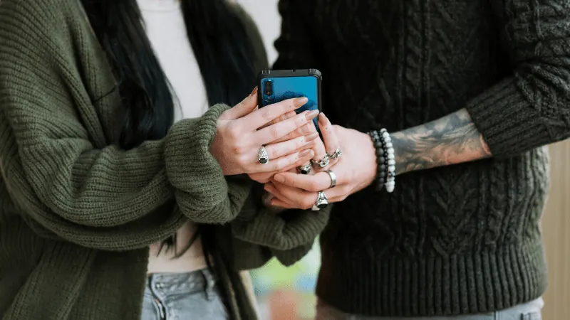 Young women using a smartphone for social media or communication, wearing casual sweaters and jewelry, close-up of hands and