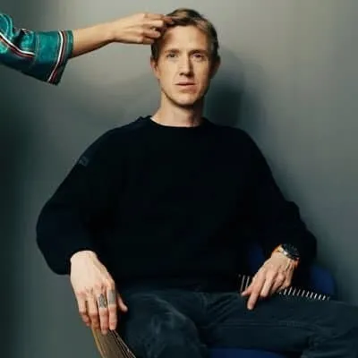 Young man sitting in a casual setting with a thoughtful expression, experiencing a stylistic makeover, new hairstyle, and fas