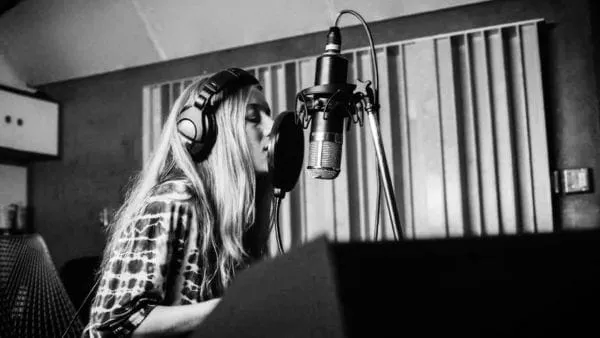 Recording artist singing into a professional microphone in a music studio for digital music production and industry insights.