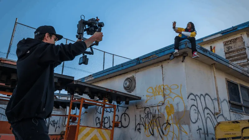High-angle shot of a videographer filming a person sitting on a graffiti-covered rooftop during sunset, capturing urban cultu