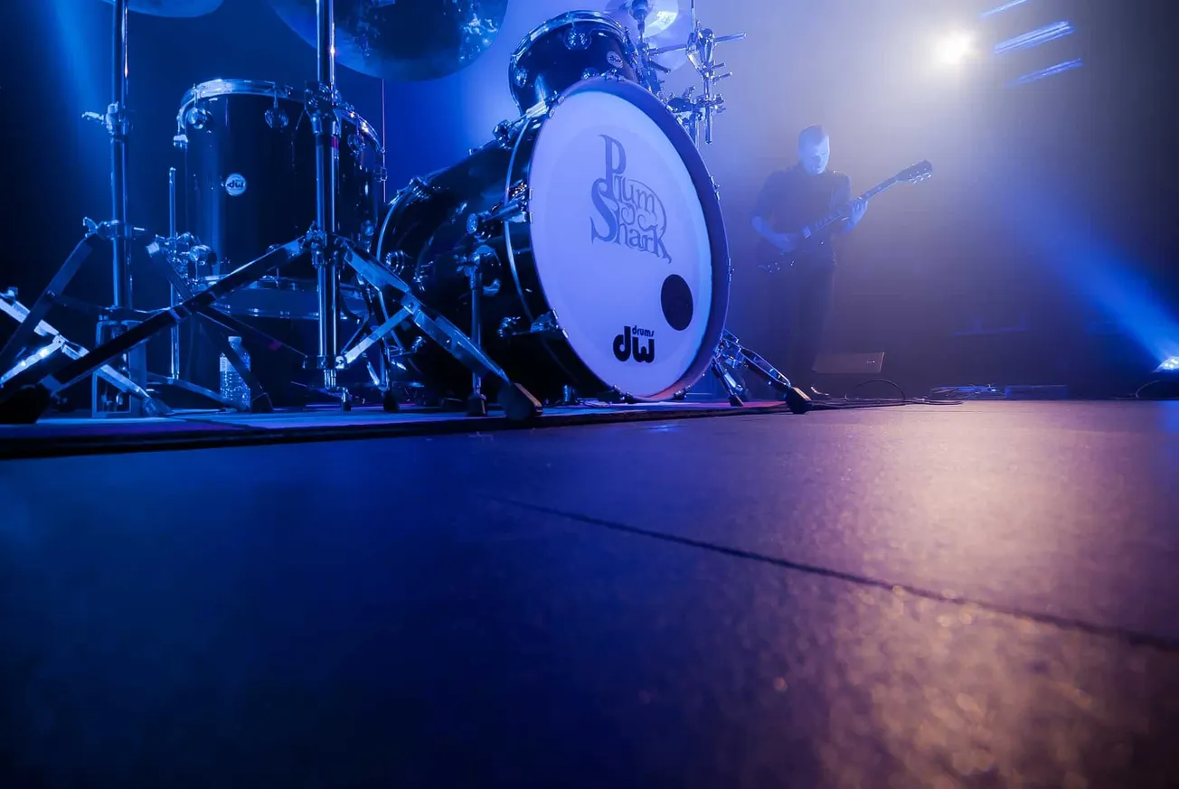 Vivid shot of a drum set featuring a bass drum with "Drum & Shank" logo, illuminated with dynamic blue and purple stage light