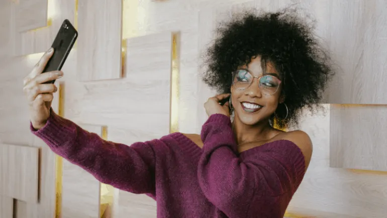Selfie of a smiling woman with curly hair wearing a purple sweater taking a photo with her smartphone at Hypebot event.