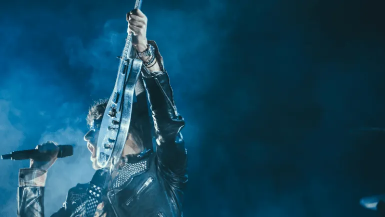 Rock musician performing with electric guitar on stage at concert under blue lights.