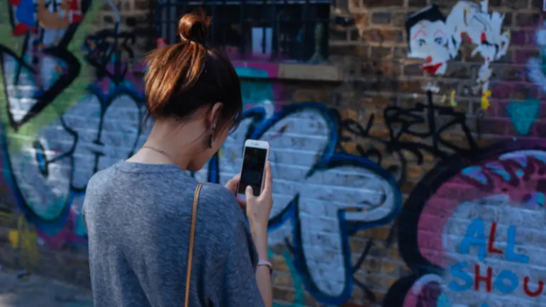 Woman using smartphone in front of graffiti wall with colorful street art and murals, urban scene, girl browsing mobile devic