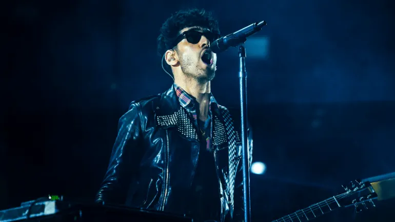 Music performer singing into microphone at concert, stage lighting, musician in leather jacket with guitar.