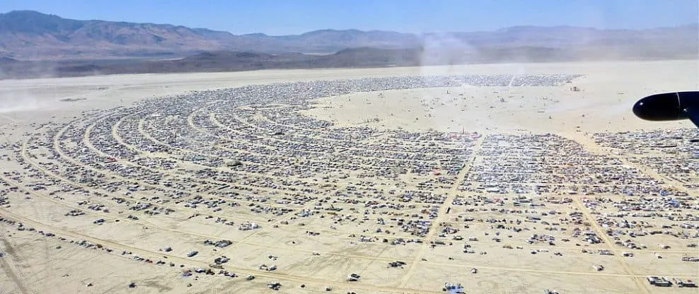 Large desert parking lot with hundreds of vehicles arranged in a circular pattern, aerial view showcasing organized event or