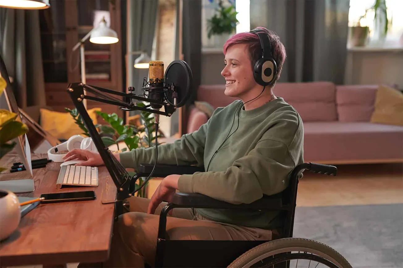 Young woman in wheelchair recording podcast with professional microphone in cozy home office setup, emphasizing accessibility