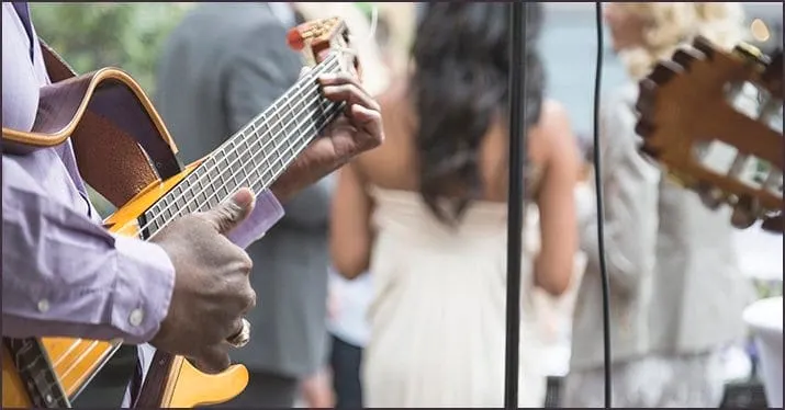 Guitarist playing outdoors at an event, with people in the background, capturing live music performance and entertainment at