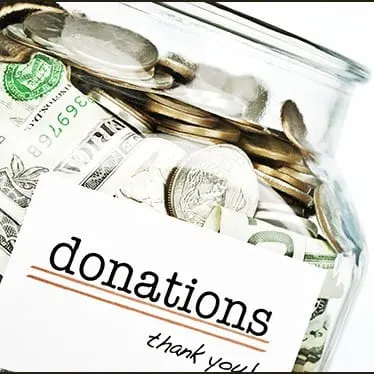 Money and coins inside a transparent donation jar with a label reading "donations, thank you" for charitable contributions an