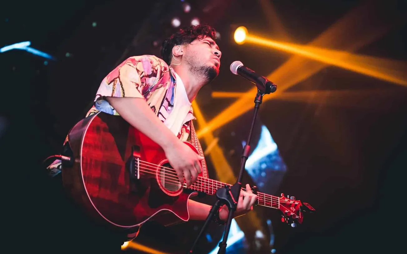 Creative musician performing live with guitar on stage under colorful lighting at a music event.