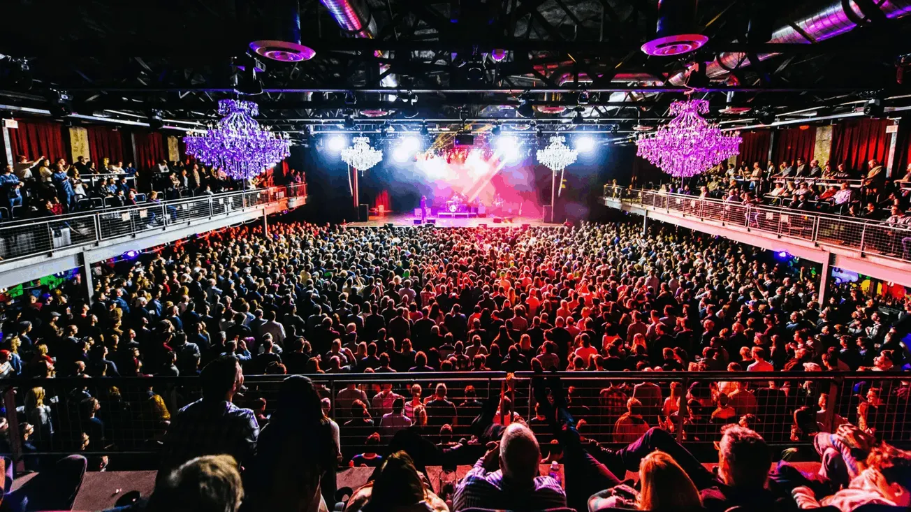 Bright concert crowd enjoying a live music event with vibrant stage lighting and elaborate chandeliers, emphasizing the inter