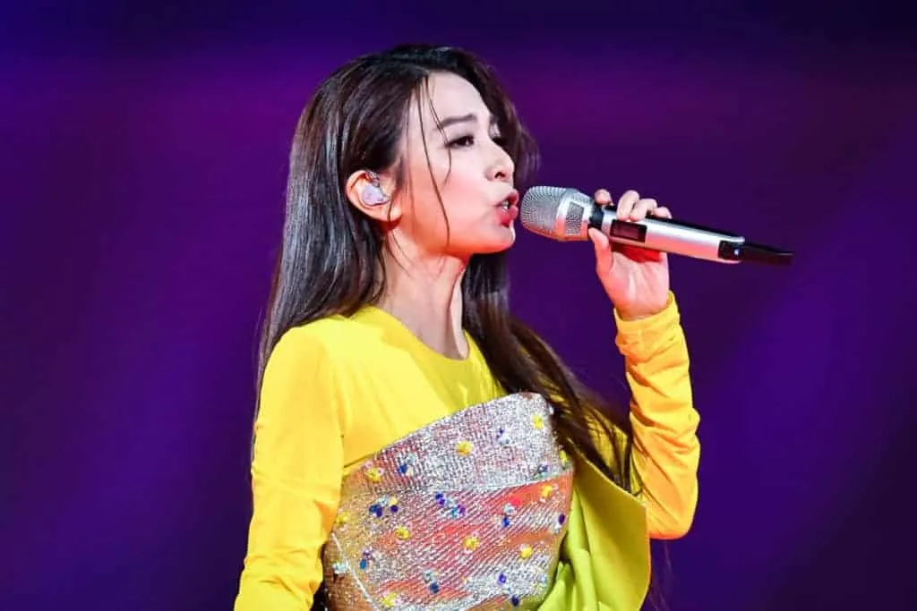 Young female singer performing on stage with a microphone, vibrant yellow outfit and stage lighting.